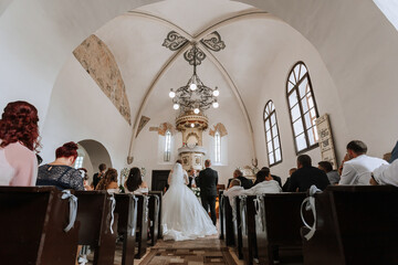 A wedding ceremony is taking place in a church with a bride and groom standing in front of the...