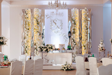 A wedding reception with a white theme. The tables are set with white tablecloths and flowers. The room is decorated with white flowers and a large mirror