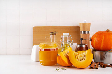 Pumpkins cooking background with sliced and whole pumpkin halves or butternut squash, raw herbs. spices on white background with cutting board, herbs, honey. Thanksgiving dinner seasonal cooking