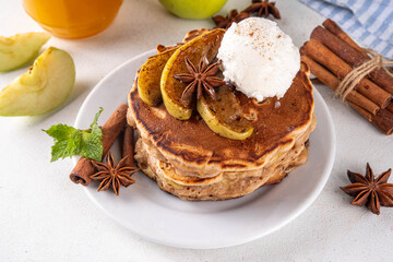 Sweet autumn apple pie pancakes stack with ice cream and caramelized apples on top, won kitchen table with spices, apples and honey jar, copy space