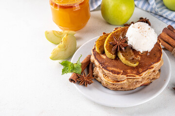 Sweet autumn apple pie pancakes stack with ice cream and caramelized apples on top, won kitchen table with spices, apples and honey jar, copy space