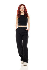 Obraz premium Charming young redhead woman posing in studio in black short blouse and black trousers on a white background
