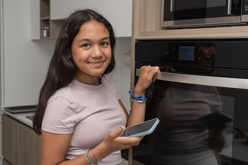 Beautiful teenager looking information with the mobile phone to make a homemade recipe at home. Looking to the camera.
