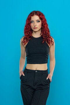 Charming young redhead woman posing in black short blouse and black trousers on a blue stdio background