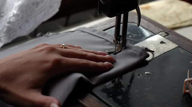 Hands deftly operate the mechanisms of a vintage sewing machine, showcasing the skilled craft of garment making and the timeless appeal of handmade textiles.