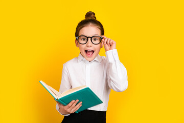 Photo of cute schoolgirl touch eyewear hold book empty space wear uniform isolated on yellow color background