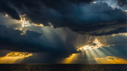 Dramatic dark storm clouds with emerging sunlight rays over a vast green field and distant horizon.