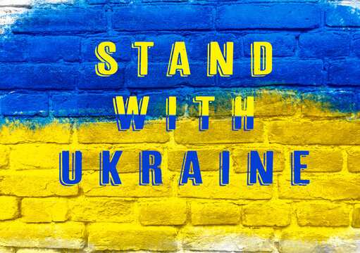 A blue and yellow brick wall with the words Stand with Ukraine written on it