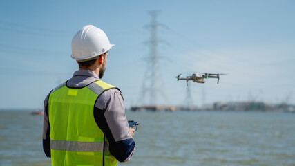 Engineer in a safety vest operating a drone to inspect and survey electrical power lines....