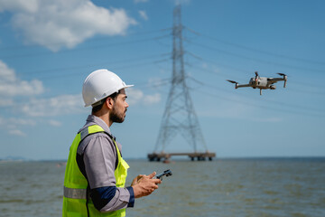Engineer in a safety vest operating a drone to inspect and survey electrical power lines. Technician inspecting the power station for scheduled maintenance.