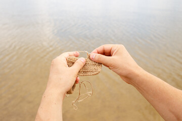 a man crochets an eco-friendly washcloth from flax jute on vacation on the shore of the lake.. Zero waste concept. Knitting as a way of relaxation. Eco-friendly solutions for everyday life.
