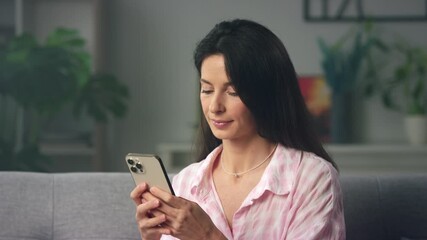 Smiling woman on sofa using smartphone at home