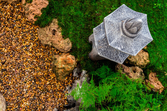 Minimal Japanese garden in home with small stone lantern and bamboo fountain and moss and flowers.
