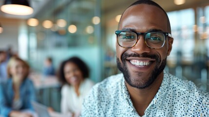 A man in glasses is smiling warmly in a meeting, with colleagues engaging positively in the background, indicating a collaborative and constructive work atmosphere.