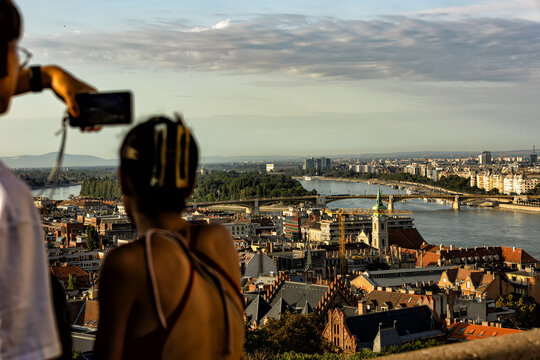 Two tourists capture memories with a smartphone overlooking the historical cityscape and scenic river. These authentic travel moments inspire a deep appreciation for diverse cultures and urban discove