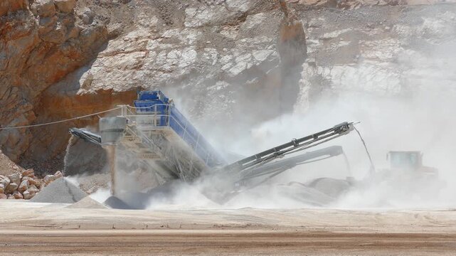 Stone crushing machine at open pit mining and loader working. Processing plant for crushed stone. Piles of gravel stone and conveyor belts. Industrial building materials, sand and gravel