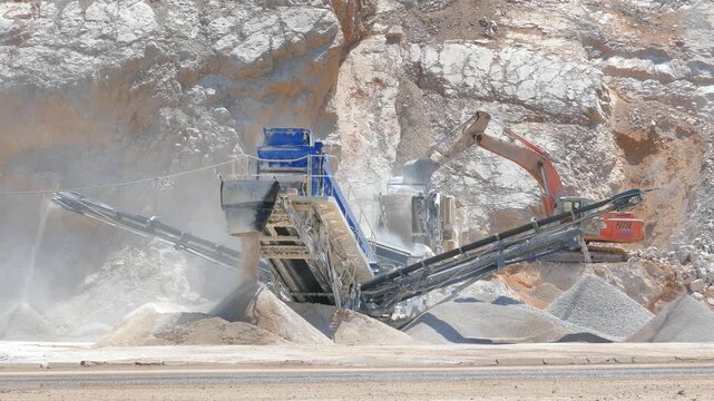 Stone crushing machine at open pit mining and processing plant for crushed stone. Piles of gravel stone and conveyor belts. Excavator loading rocks. Concepts of industry and building materials
