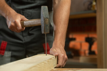 A person skillfully positions a nail against a piece of wood, preparing for a precise hammering technique. The focus is on the careful alignment needed for effective and accurate nailing as they bring
