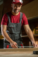 A person in a red outfit meticulously measures a piece of wood using a tape measure while working...