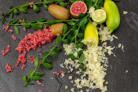 Ripe yellow and burgundy oblong citrus fruits with green sprigs on the black slate slab, close-up. Australian finger lime plant indoor growing. Microcitrus australasica, Faustrimedin