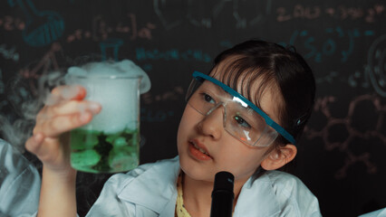 Young girl holding green chemical solution and inspect carefully while sitting in front of...
