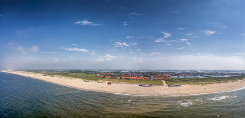 A panoramic view showcases a lengthy beach bordered by the ocean on one side and a town featuring red rooftops on the other.