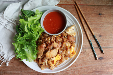 Khua kai, Stir-fried rice noodle with chicken meat in Thai style serve with fresh vegetable and shiracha sauce. Authentic Thai food.