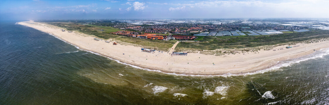 A panoramic view of Ter Heijde village shows an expansive sandy beach curving around a body of water, with buildings and farmland visible in the background. 