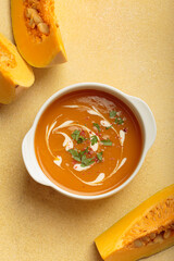 Creamy pumpkin soup bowl on warm yellow beige background with parsley and pink pepper, a cozy...