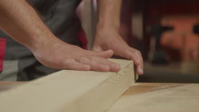 Close-up of an experienced carpenter, a man runs his hand over the wood that he has sanded.