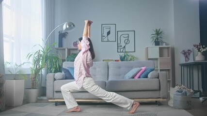 Yoga woman in plant-filled living room practicing warrior pose