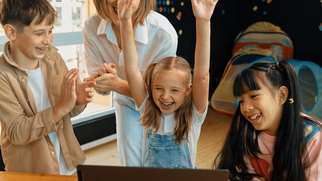 Caucasian teacher and happy students clapping hands to celebrate successful project writing engineering code or prompt by cute smart learner sitting at laptop in STEM technology classroom. Erudition.