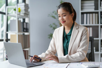 Asian businesswoman is smiling while working on her laptop and analyzing financial data