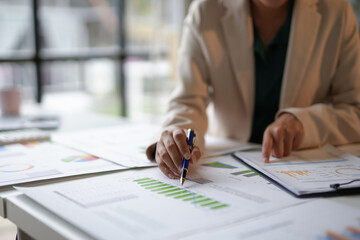 Businesswoman is analyzing financial charts and business data on a table, using a pen to point at a graph