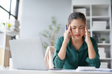 Young businesswoman is feeling tired and having a headache, touching her head, while working on a laptop computer at the office