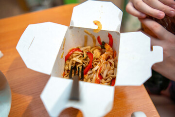 cardboard box cradles a vibrant stir-fried noodle dish, bursting with colorful vegetables and...