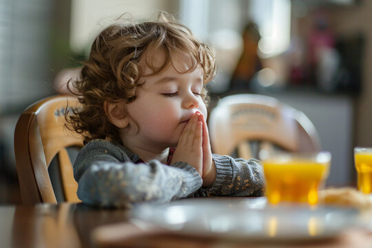 Young boy child praying at kitchen table before meal