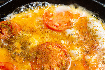 Eggs with tomatoes circles and onions in a pan are fried in oil
