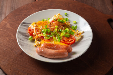 Eggs with tomatoes and fried sausage in a plate on a round wooden stand