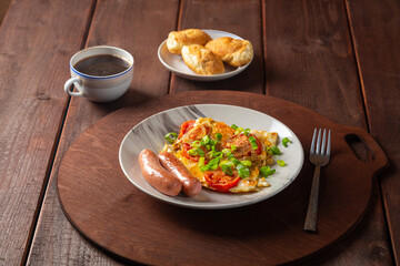 Eggs with tomatoes and fried sausage in a plate on a wooden table of coffee and croissants on a round stand