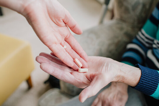 A care person hands pills to an elderly woman in a care facility. - Powered by Adobe