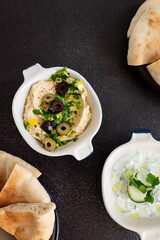 Tzatziki sauce and hummus. Gray grunge background. Greek sauce made from yogurt and vegetables, traditional hummus with olives. Top view, flat lay, copy space