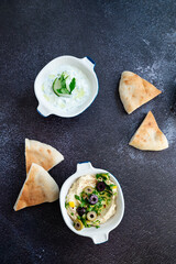 Tzatziki sauce and hummus. Gray grunge background. Greek sauce made from yogurt and vegetables, traditional hummus with olives. Top view, flat lay, copy space