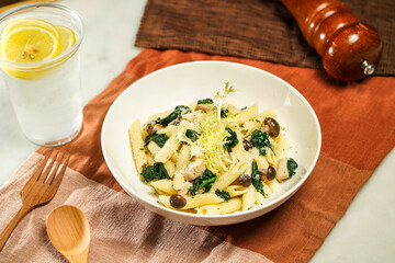 Penne with Spinach and Mushroom with lemonade, wooden spoon and fork served in plate isolated on napkin and dining table side view of italian food