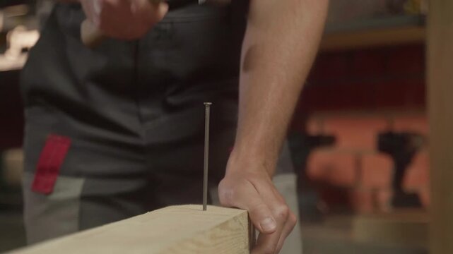 A person skillfully positions a nail against a piece of wood, preparing for a precise hammering technique. The focus is on the careful alignment needed for effective and accurate nailing as they bring
