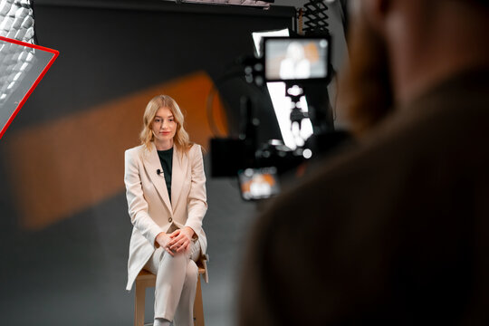 A professional woman wearing a business suit is being filmed in a studio setting
