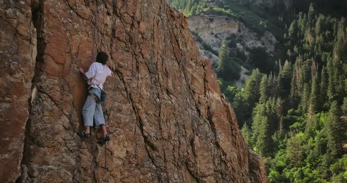 Young man climbing on rocky cliff in Utah canyon - drone shot moving out