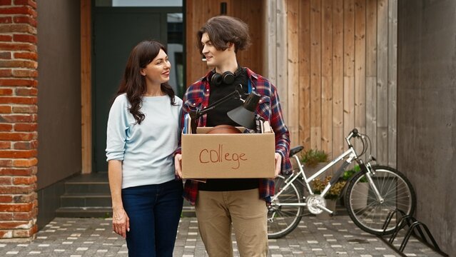 Portrait of adult preaty woman and young boy standing outside and looking at camera with smile. Mother hugs her son leaving parents' house. Cute guy entering university and moving away from home.
