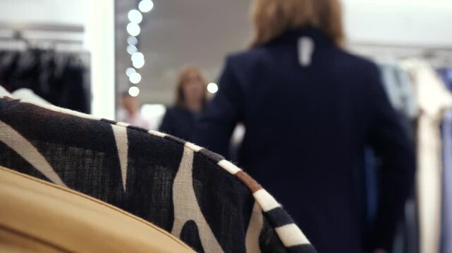 Young woman trying on jacket or clothes in clothing store and looking in mirror