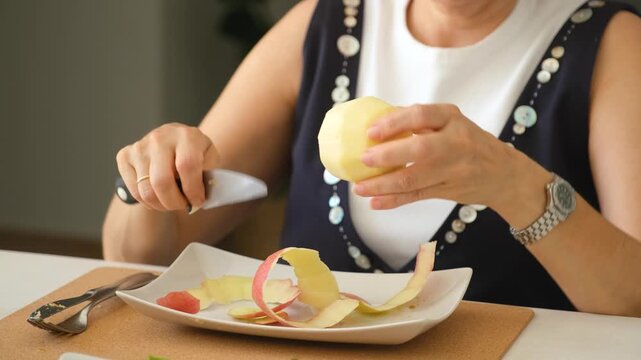 Middle aged woman peeling and slicing an apple, then eating a slice in a modern home. Step by step sequence showcasing apple preparation